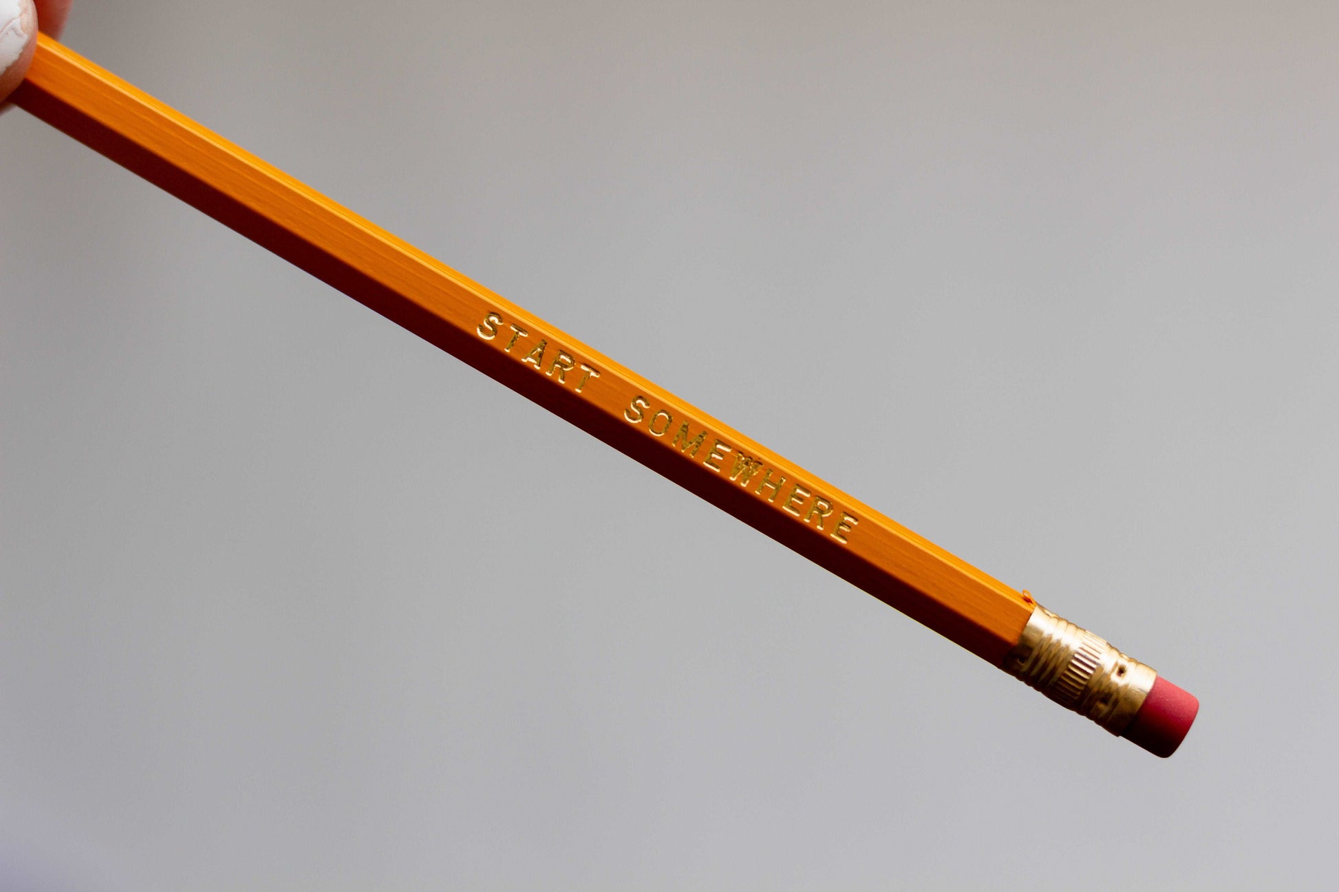 A closeup image of the yellow #2 lead free pencil with pink eraser that has foiled engraved imprint that says start somewhere