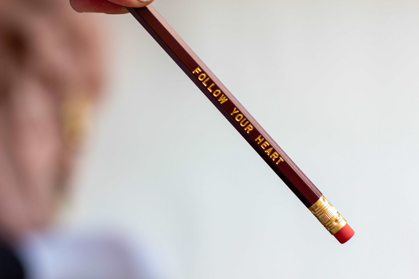 A closeup of the dark red #2 lead free unsharpened pencil with pink eraser and foil engraved imprint that says follow your heart.